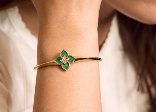 Gold bracelet with green flower charm on wrist