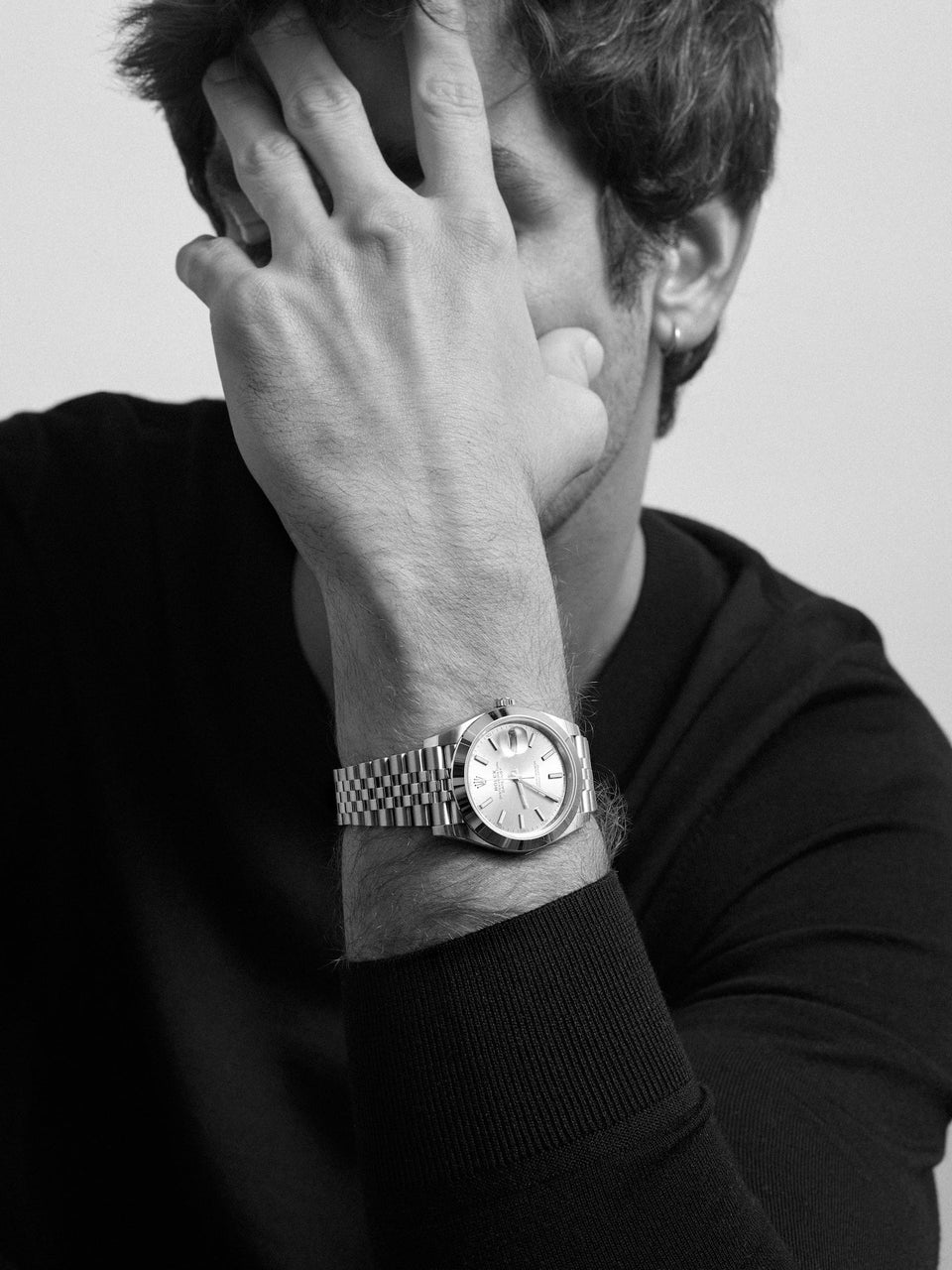 Man covering face with hand, wearing watch.